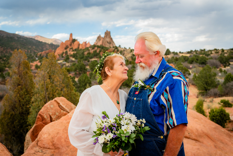 Elopement Photographer, Older couple gaze at each other on top of red rocks and near vegetation, she holds bouquet