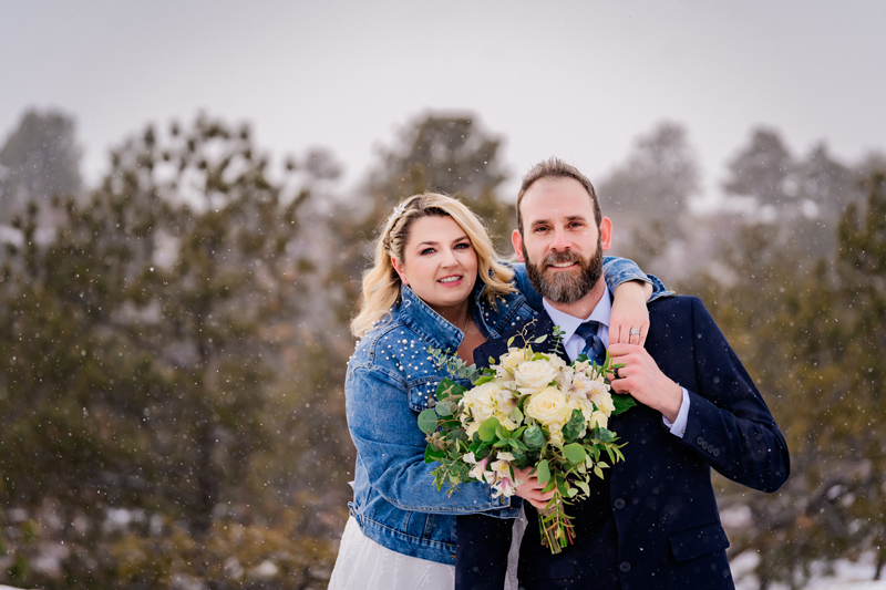 Elopement Photographer, man and woman hold a bouquet together, her hand wrapped around him near the forest